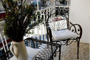 A balcony with a white vase of green plants, a metal chair with a cushion, and a metal table.