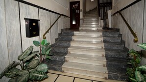 Una escalera de mármol con barandillas negras y doradas, que conduce a una puerta con un cartel encima.