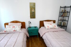 Une chambre avec deux lits, chacun agrémenté de draps à motifs floraux, et une table de chevet turquoise placée entre les deux.