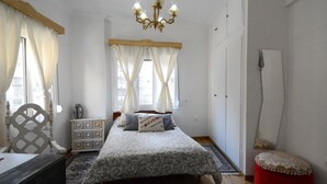Un dormitorio con cama, cómoda, silla, espejo y un reposapiés rojo.