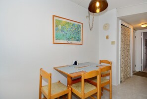 A dining area with a table and four chairs, a framed artwork on the wall, a clock, and a door leading to another room.