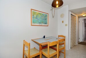 A dining area with a table, four chairs, a framed painting, a clock, and a door leading to another room.