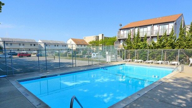 Une piscine rectangulaire avec un escalier en métal, entourée d’une clôture en treillis métallique.