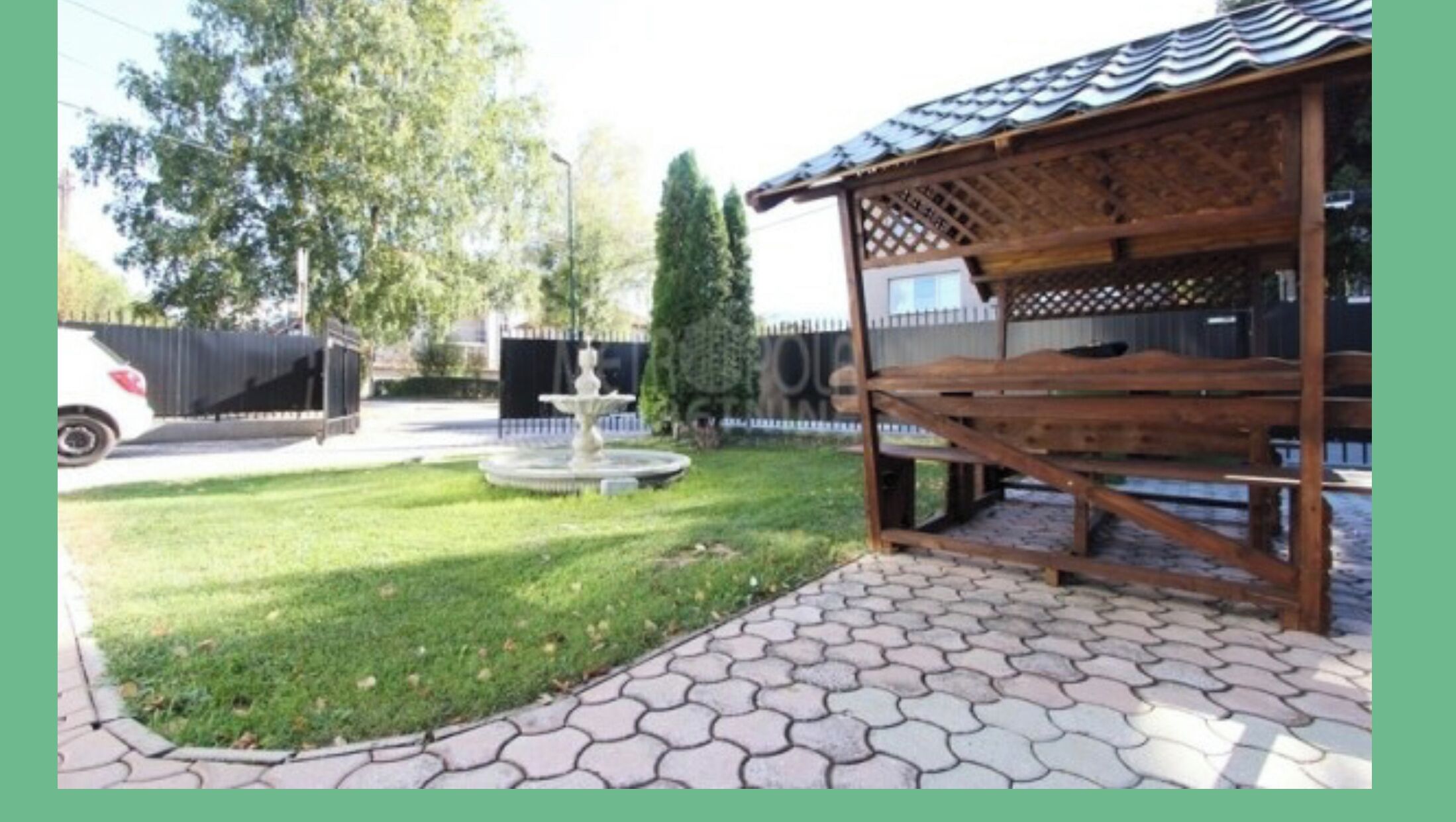 A wooden gazebo with a tiled roof, a fountain, and a paved walkway.