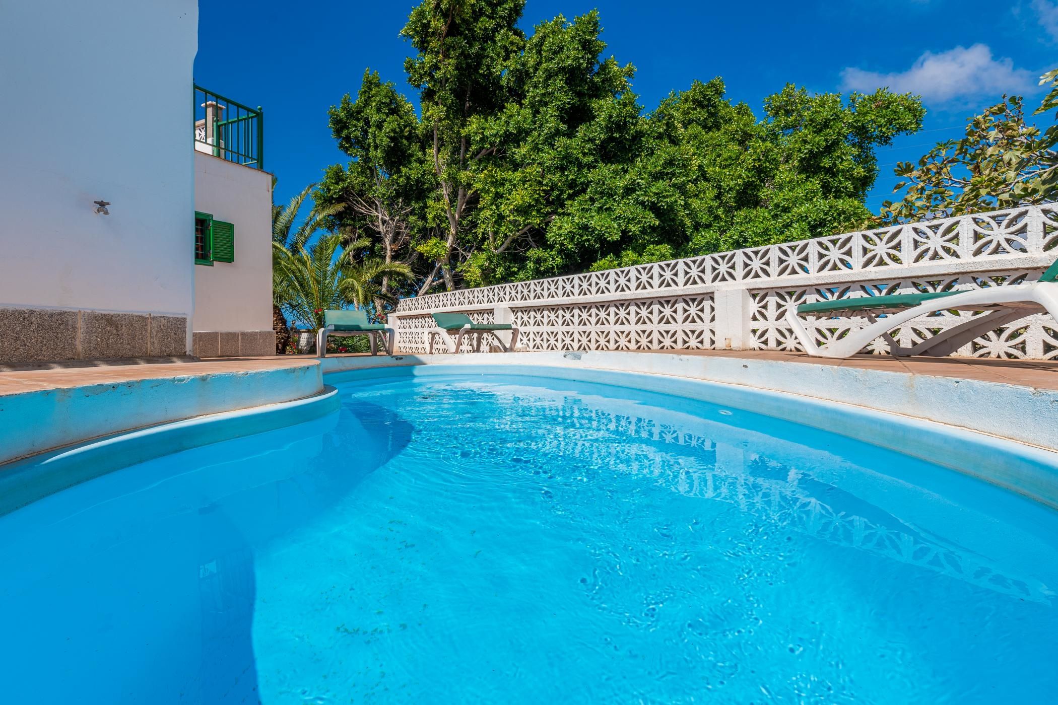 A clear blue pool with a white fence and a building with green shutters.
