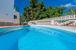 A clear blue pool with a white fence and a building with green shutters.