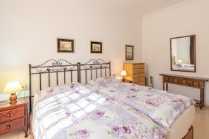 Ein Schlafzimmer mit Bett, Nachttischen, einem Schminktisch, einem Spiegel und gerahmten Bildern an der Wand.