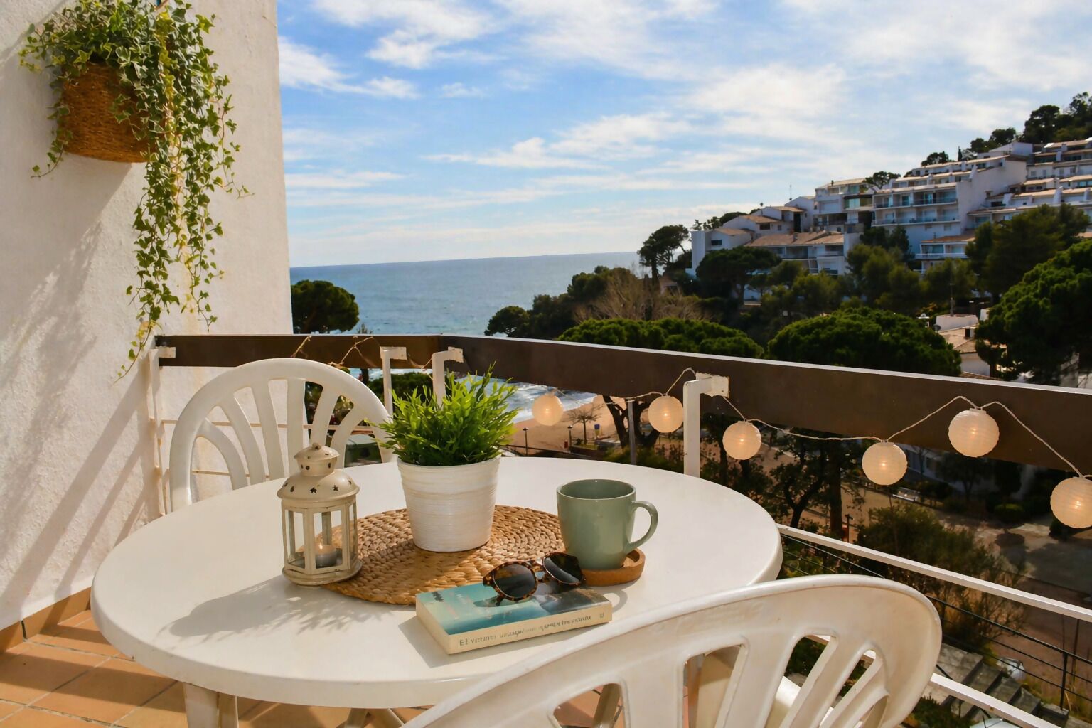 Ein Balkon mit Tisch, Stühlen, einem Blumentopf, einer Laterne und einem Buch.