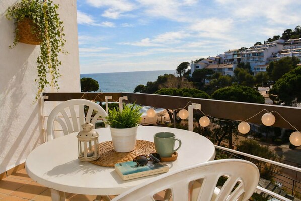 A balcony with a table, chairs, a potted plant, a lantern, and a book.