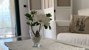 Et glasbord med et blondeborddække, en vase med hvide blomster og et dekorativt glasværk.