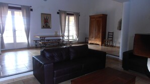 A spacious living room with a black leather sofa, a wooden coffee table, and a dining table with chairs. There is a large wooden cabinet and a painting on the wall. - AIR-CONDITIONED VILLA WITH HEATED POOL AND BREATHTAKING VIEW (Draguignan)