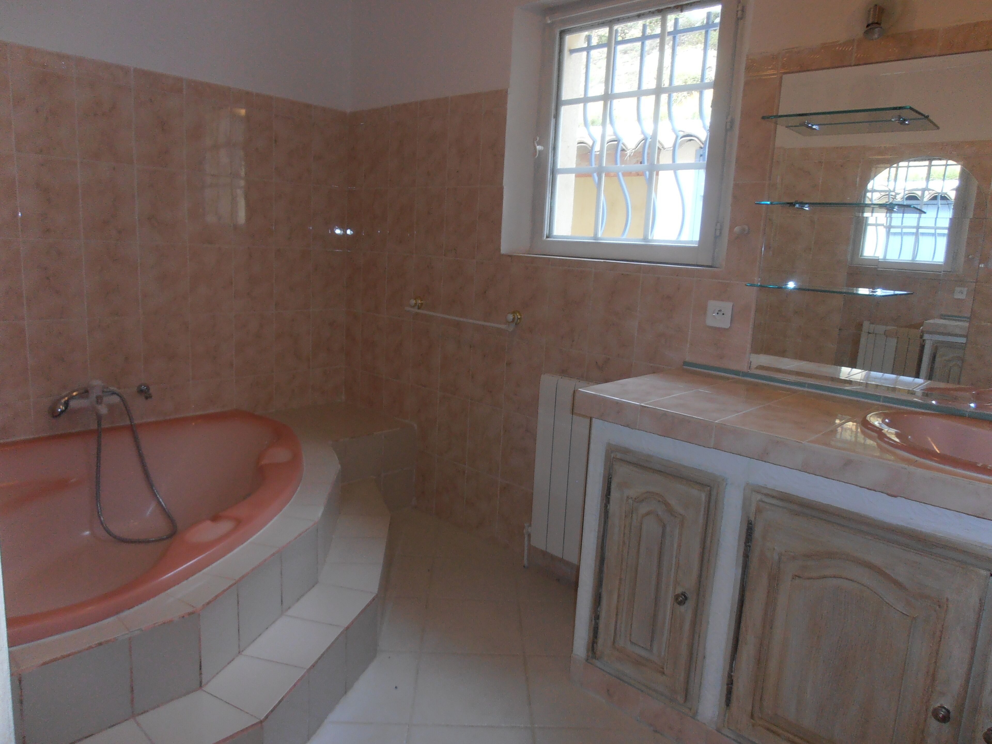 A bathroom with a freestanding bathtub, a vanity with a mirror, and a window with bars.