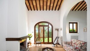 A spacious living room with a fireplace, a sofa, and a large arched doorway leading to a garden.