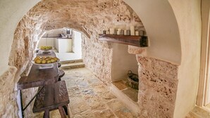 Ein schmaler Stein-Korridor mit einer rustikalen Steinwand, einem Holztisch mit Früchten und einem Steinkamin.