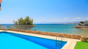 A swimming pool with a stone border, a metal ladder, and a view of the sea and mountains in the background. - FANTASTIC BEACH FRONT APARTMENT IN SALOU 068 BAHIA (Salou)