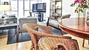 A living room with wicker furniture, a television, a bookshelf, and a dining table.