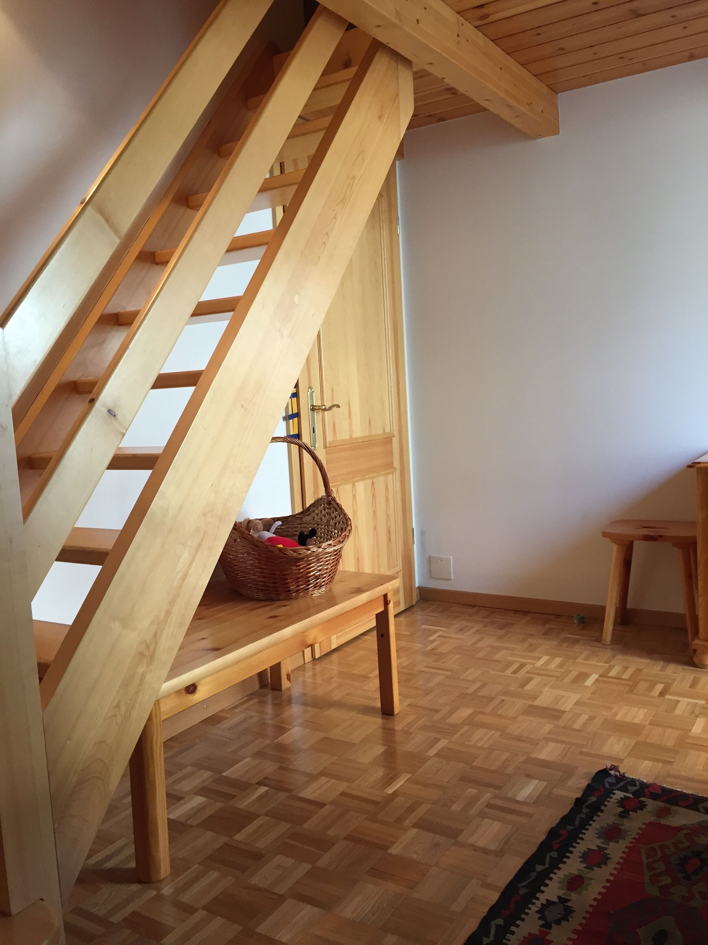 A wooden staircase with a bench underneath, a small table, and a patterned rug on the floor.