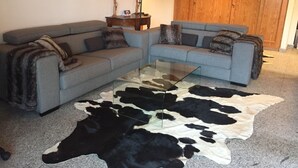 Una sala de estar con dos sofás grises, una mesa de centro de vidrio y un tapete de cuero de vaca blanco y negro.