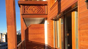 Un balcón de madera con un diseño geométrico de baldosas, amplios ventanales correderos y vistas de la ciudad.