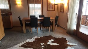 Un comedor con una mesa y sillas, un tapete de cuero de vaca y una cocina al fondo.