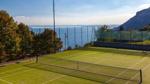 Una cancha de tenis con red, rodeada de árboles y vista al mar.