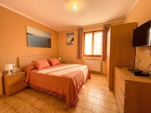A bedroom with a bed, nightstand, dresser, TV, and a window with curtains. - Appartamento Petra Tignale (Tignale)