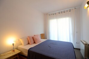 Een slaapkamer met een bed, bedlamp en een raam met gordijnen.