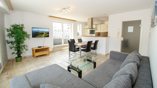Een moderne woonkamer met een bank, een glazen salontafel, en een eetgedeelte met stoelen en een tafel.
