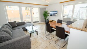 Een moderne woonkamer met een bank, salontafel, eettafel, stoelen en een potplant.