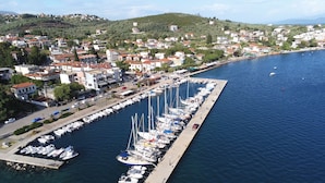 A marina with numerous boats docked along a pier, surrounded by residential buildings and a hilly landscape in the background.