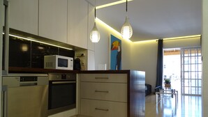 A modern kitchen with stainless steel appliances, a microwave, and a coffee maker. There is a dining area with a table and chairs visible through an open door.