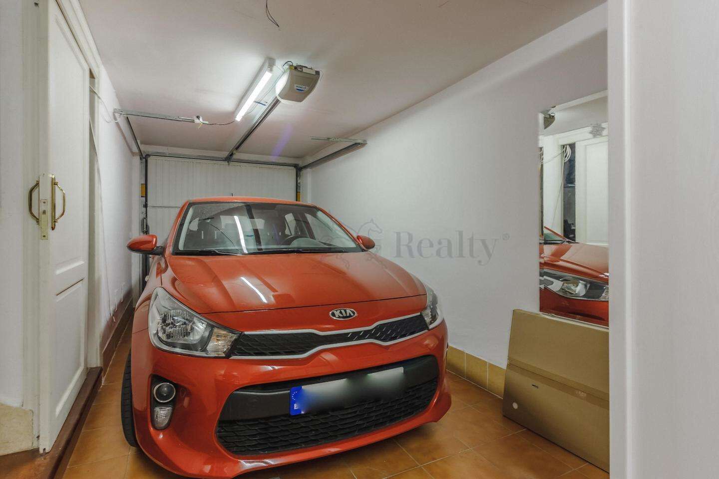 Un coche rojo estacionado en un pasillo estrecho con paredes blancas y suelo de baldosas.