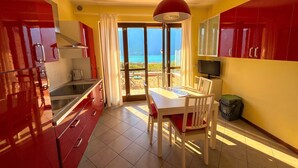 A modern kitchen with red cabinets, a dining area with a table and chairs, and a view of the sea through large glass doors. - La Quiete 23 Holideal Apartment Lake View (Tremosine)