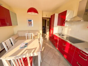 A modern kitchen with red cabinets, a dining area with a white table and chairs, and a red pendant light.