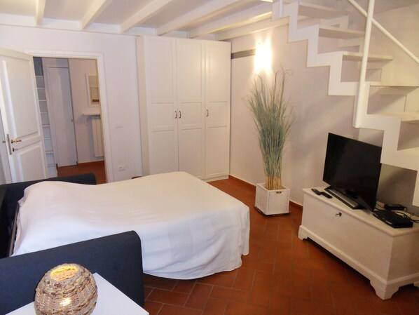A bedroom with a bed, a TV, a dresser, and a staircase.