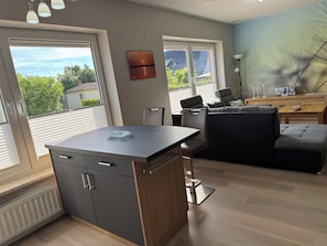 Una sala de estar moderna con comedor, un sofá, una mesa de centro y vistas al exterior a través de grandes ventanales.