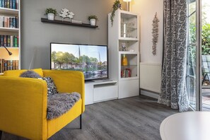 Un salon avec un canapé jaune, un téléviseur à écran plat, un meuble blanc aux portes vitrées et une vue sur un canal.