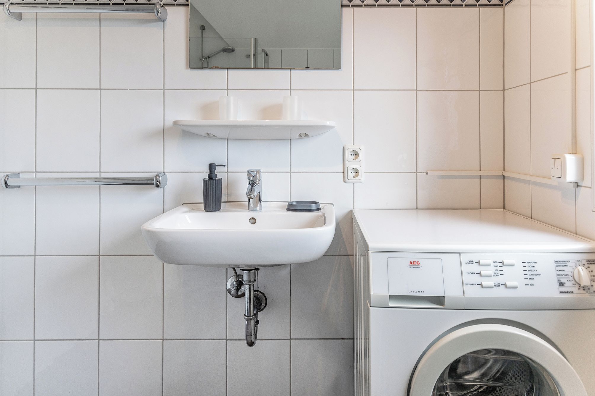A bathroom with a sink, mirror, and a washing machine.