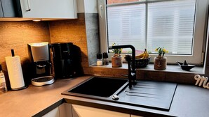 Een moderne keuken met een zwarte spoelbak, witte kastjes en een raam met zonwering.