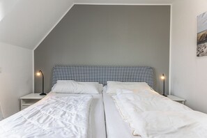 A bedroom with a sloped ceiling, two beds with white bedding, a checkered headboard, and bedside lamps. - House "dyke Rose" Quiet location, Wi-Fi, 300 meters to the beach, top is directing (Harlesiel)