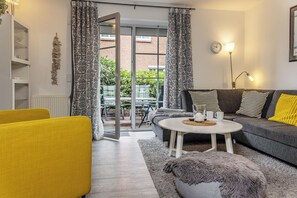 Un salon avec un canapé, un fauteuil jaune, une table basse ronde et un tapis à motifs.