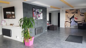 Una moderna área de recepción con una planta grande en maceta, un televisor montado y un mural en la pared.