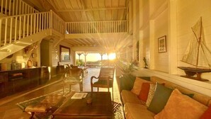 Un vestíbulo espacioso con techo alto, una escalera, una zona de estar con sofá y sillones, y vistas al exterior.