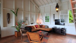 Amplia sala de estar con un sofá grande, una mesa de centro y un televisor. Se observa una silla de madera y una planta en la esquina.