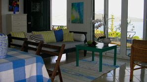Ein Wohnzimmer mit einer Couch, Sesseln, einem Tisch und Meerblick durch große Fenster.