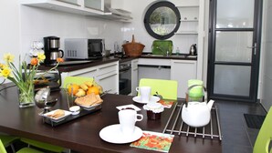 Une cuisine moderne avec des meubles blancs, une fenêtre ronde et un coin repas agrémenté d’assiettes, de tasses et d’une théière, le tout dans des tons blancs.