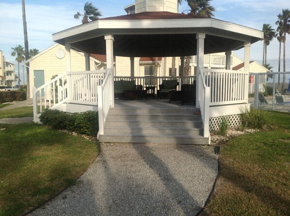 A gazebo with a concrete floor and white railings, surrounded by grass and palm trees. - "Island Time" Full Kitchen, Washer & Dryer, Close to Beach, Pool and Hot Tub! (Corpus Christi)