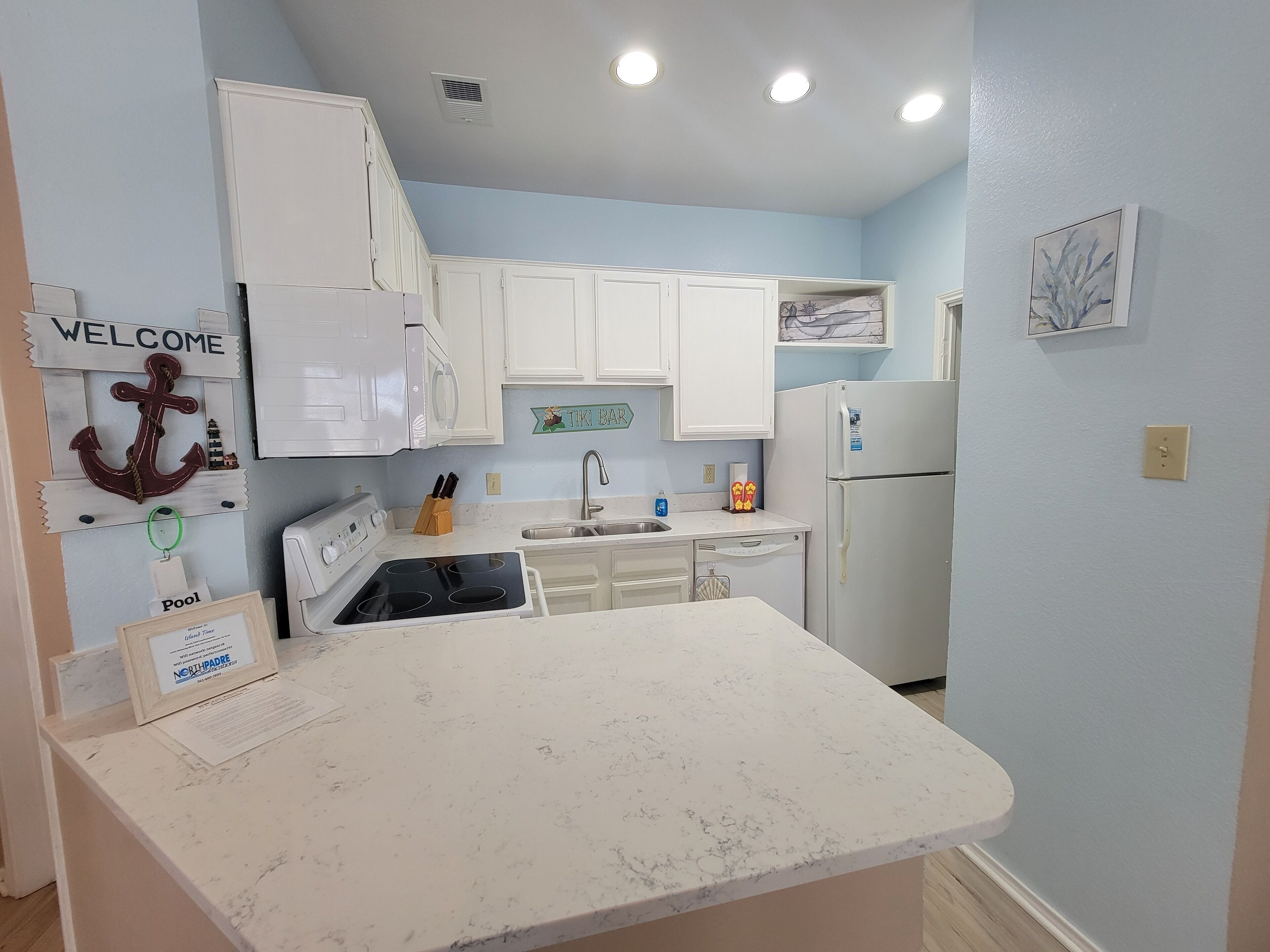 A compact kitchen with white cabinets, a white countertop, a sink, a stove, and a refrigerator.