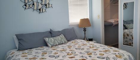 Un dormitorio con cama, mesita de noche, lámpara, decoración en la pared, ventana con persianas y armario.