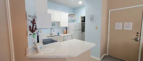 A modern kitchen with white cabinets, a stainless steel sink, and a built-in oven. There is a welcome sign and a bar sign on the wall.